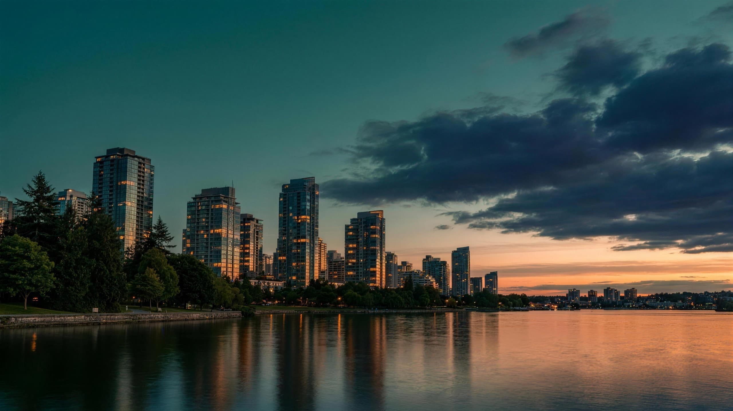 Canadian city skyline at dusk across the water, framed by green waterfront trees